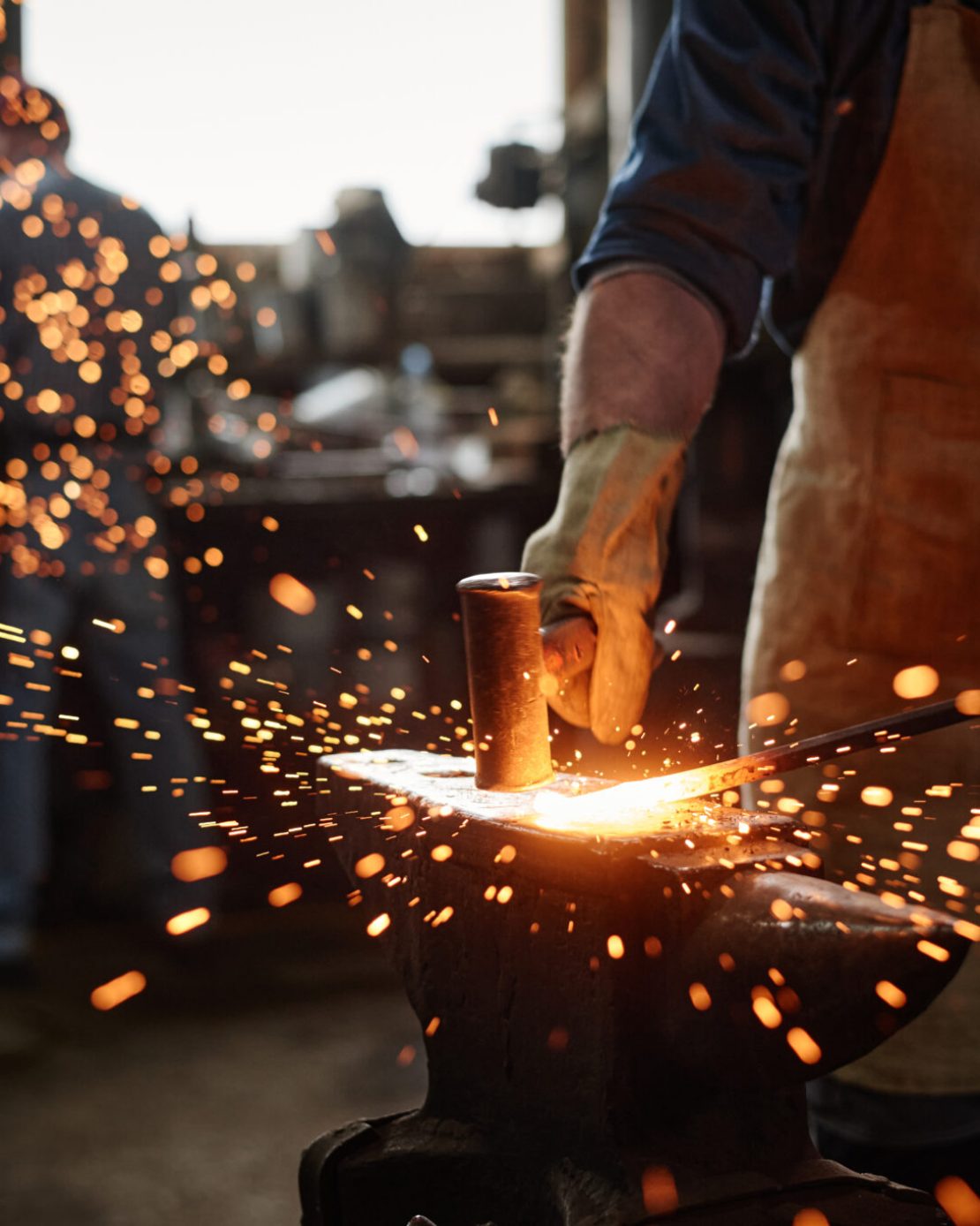 Close-up of blacksmith in apron working with hammer and iron in the workshop